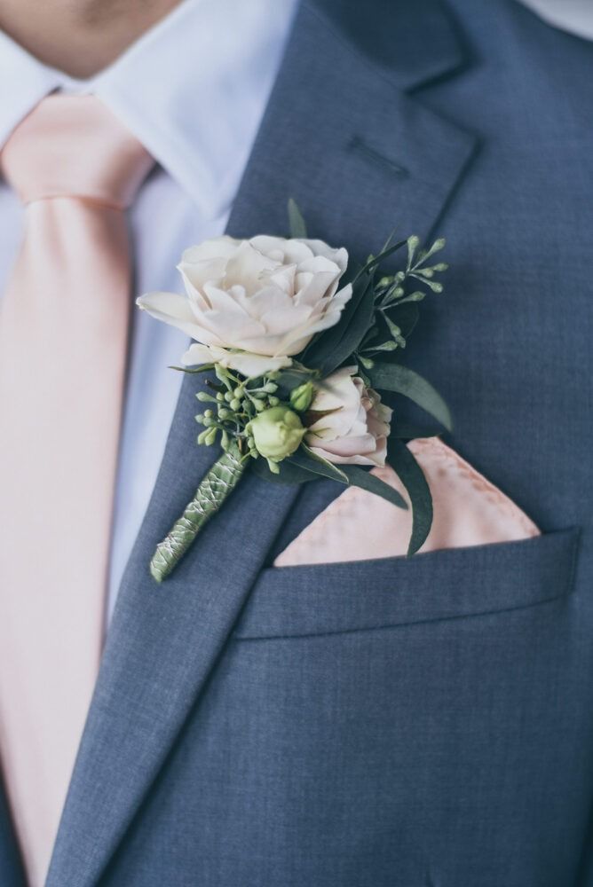 Man in a gray suit with a peach tie, pocket square, and floral boutonniere.