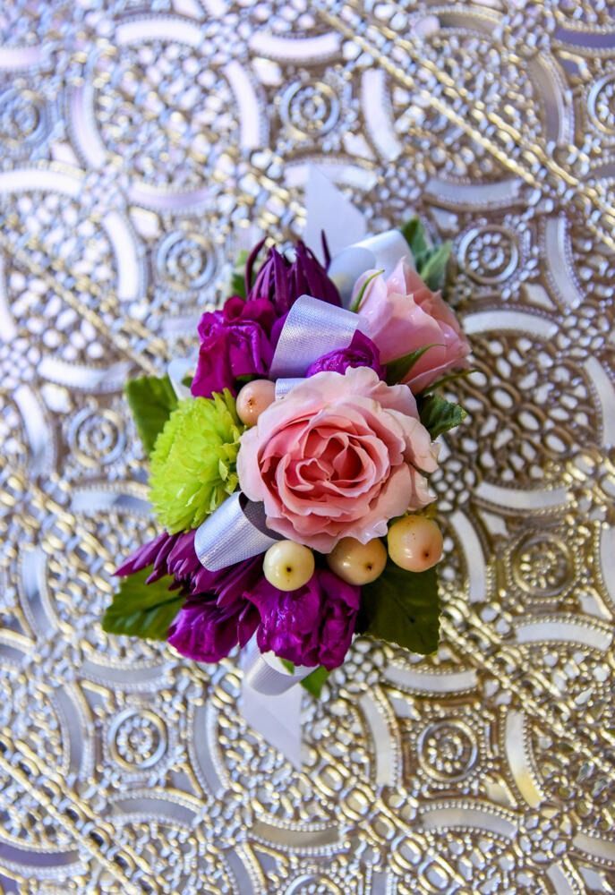 Floral wrist corsage on decorative silver surface. Pink and purple flowers with ribbon.