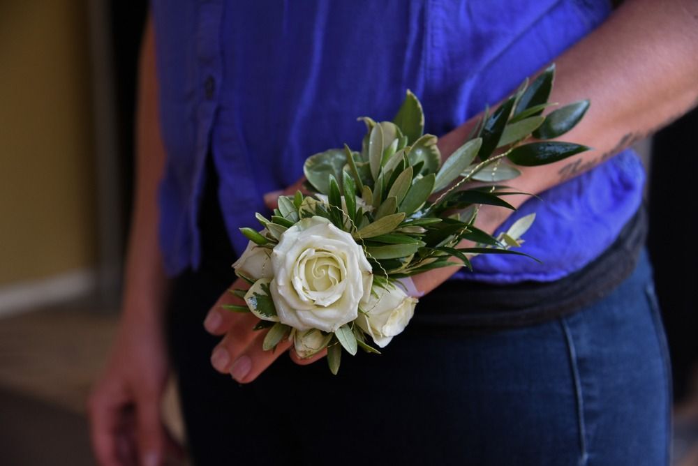 Person wearing a wrist corsage of white roses and greenery, against a blue shirt and jeans.