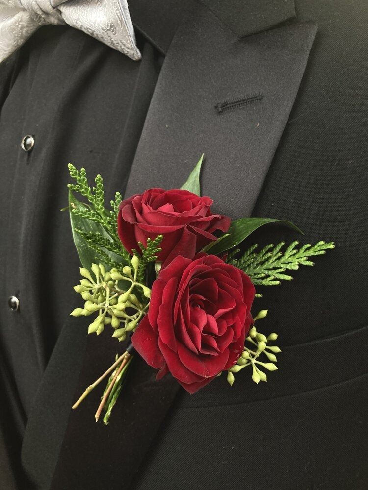 Boutonniere of two red roses with greenery on a black tuxedo.