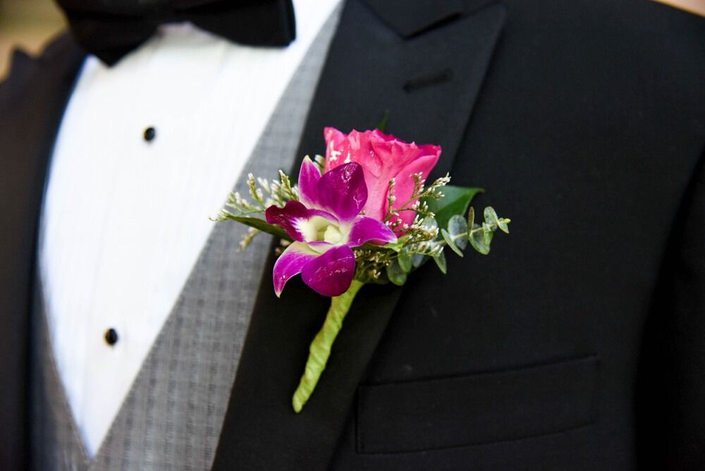 Boutonniere with pink rose and purple orchid on a black tuxedo jacket.