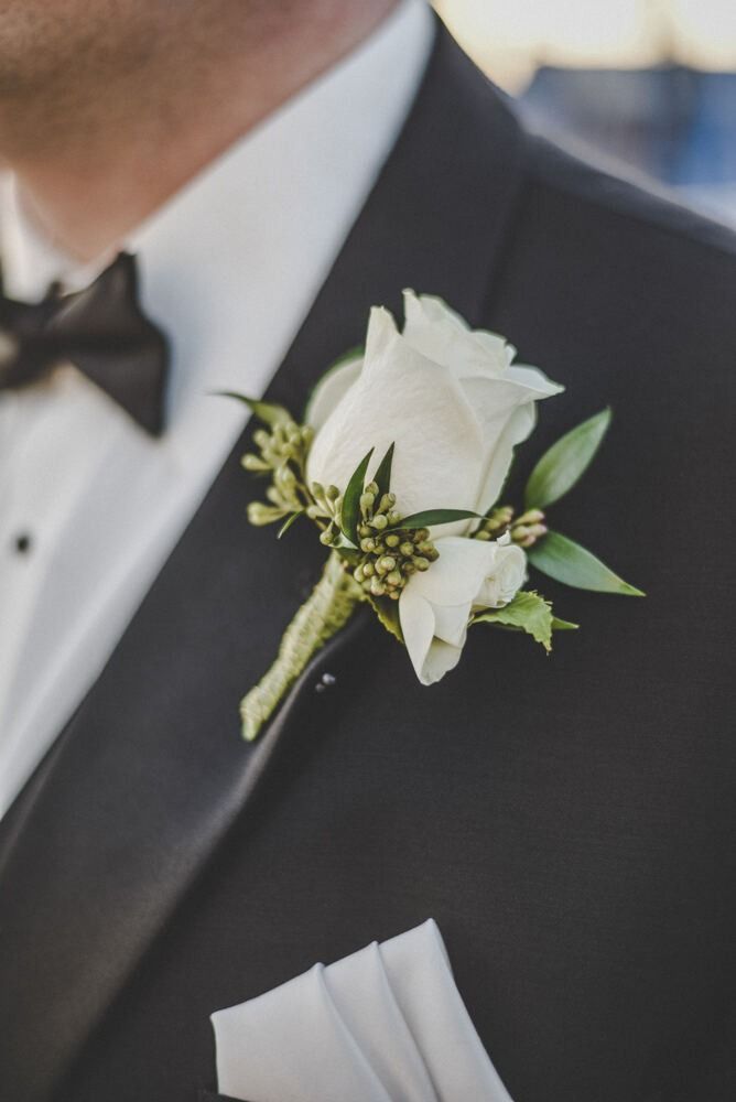 Close-up of a black tuxedo with a white rose boutonniere and a bow tie.