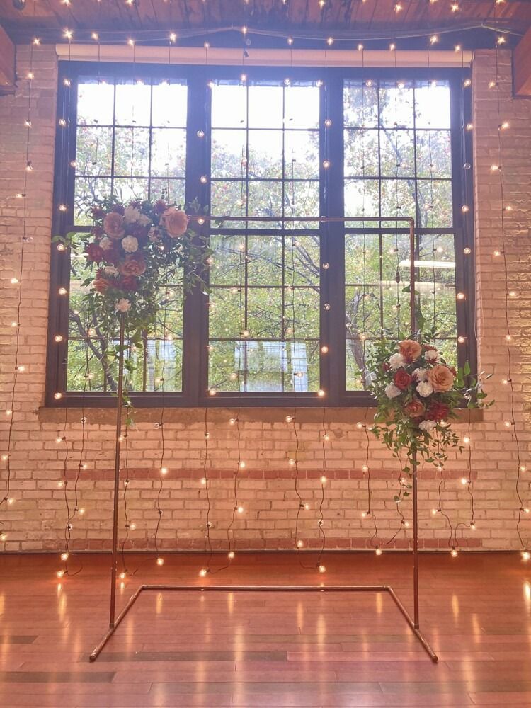 Wedding ceremony setup with floral arrangements, string lights, and a large window.