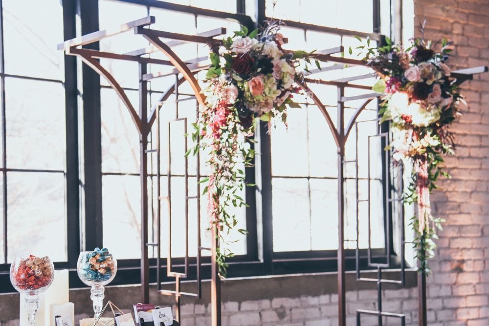 Wedding arch with floral arrangements against a window. Glass candy jars on a table in the foreground.