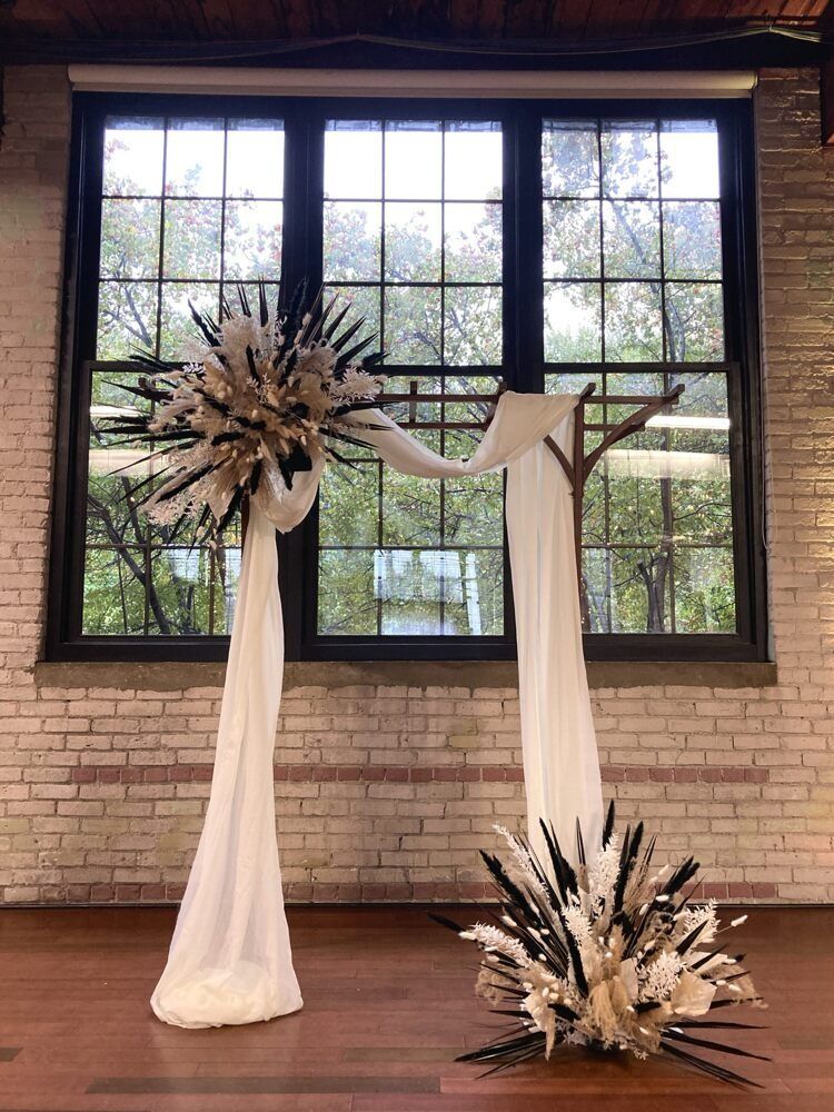 Wedding arch with white fabric, floral arrangements, and a window backdrop.