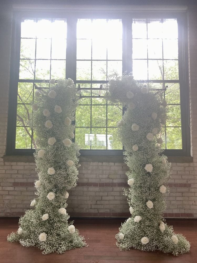 Two floral pillars covered in baby's breath and roses, flanking a window.
