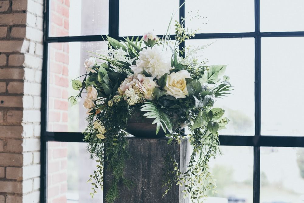 Floral arrangement with white and light pink flowers on a stone pedestal by a large window.