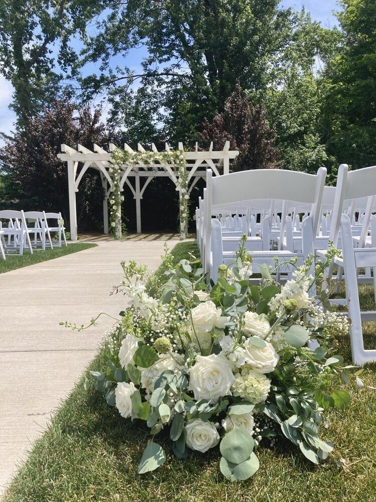 Wedding ceremony setup with white chairs, flowers, and pergola arch.