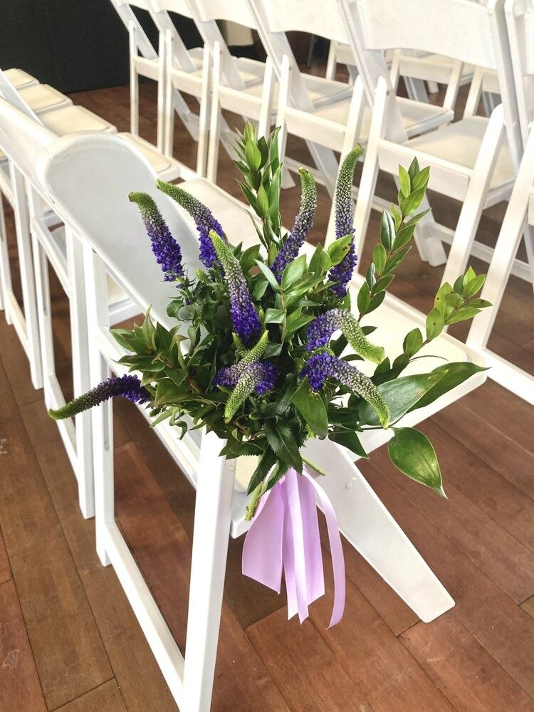 White folding chair decorated with purple flowers and lilac ribbon.