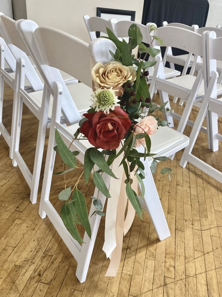 White folding chairs decorated with floral arrangements and ribbons.