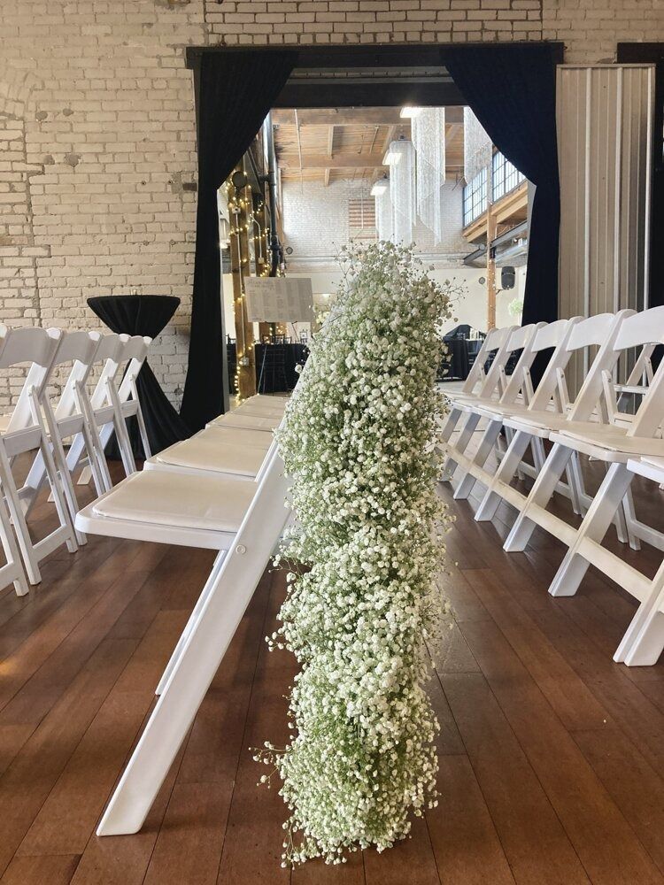 White chairs with a baby's breath floral arrangement alongside them in an indoor event space with brick walls.