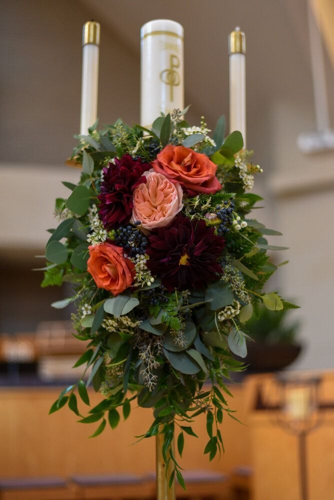 Candle arrangement with flowers, greenery, and candles in a church setting.