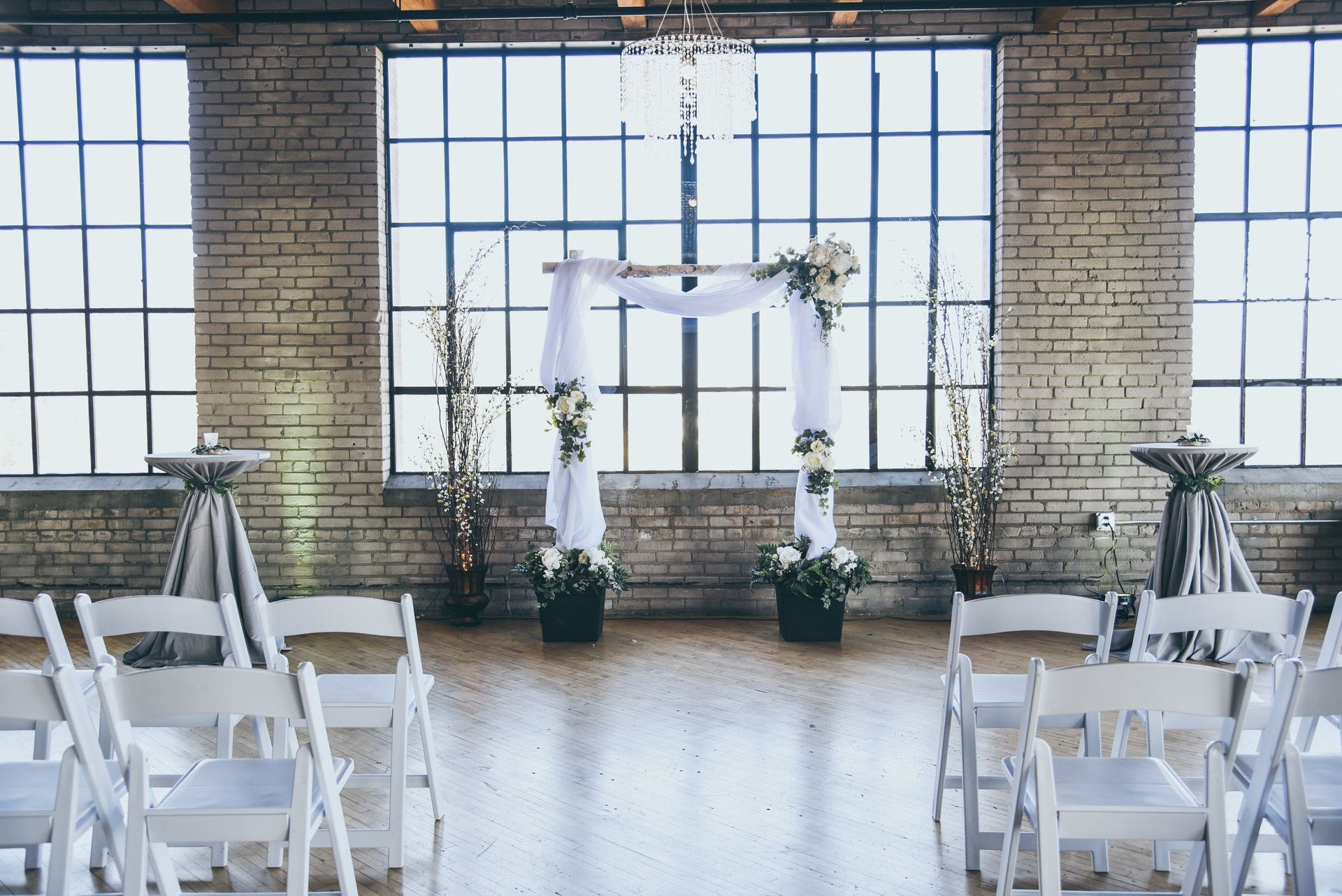 Wedding ceremony setup in an industrial space with an arch, white chairs, and large windows.