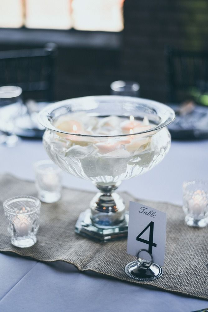 Table centerpiece with flowers in a glass bowl, burlap runner, and table number card.
