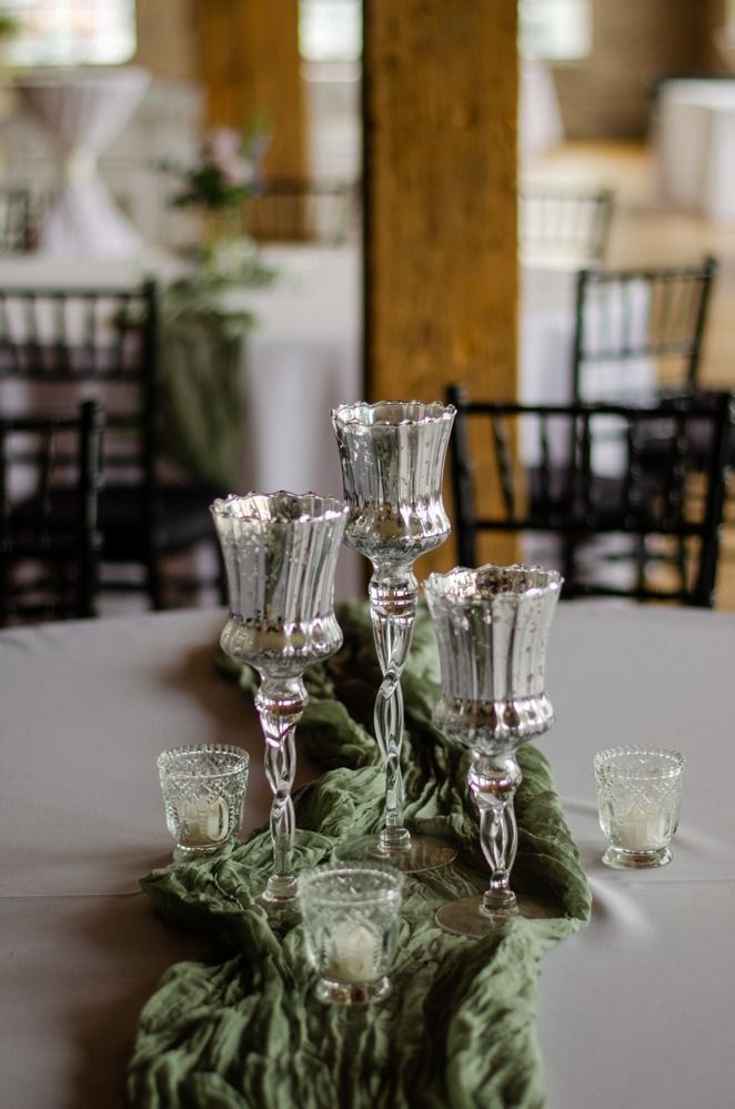 Silver candle holders and votives on a gray table runner with a green fabric centerpiece, set for an event.