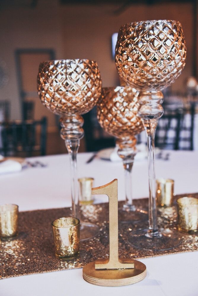 Gold table centerpiece with decorative candle holders, table number one, and a glitter runner.