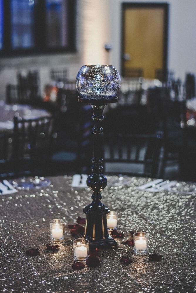 Candle centerpiece on a sequined tablecloth, with lit votives and rose petals. Dimly lit room with tables and chairs.