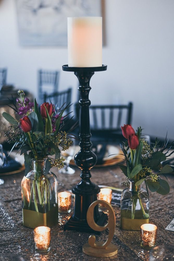 Elegant table centerpiece with tall black candlestick, red tulips, votive candles, and gold number 9.