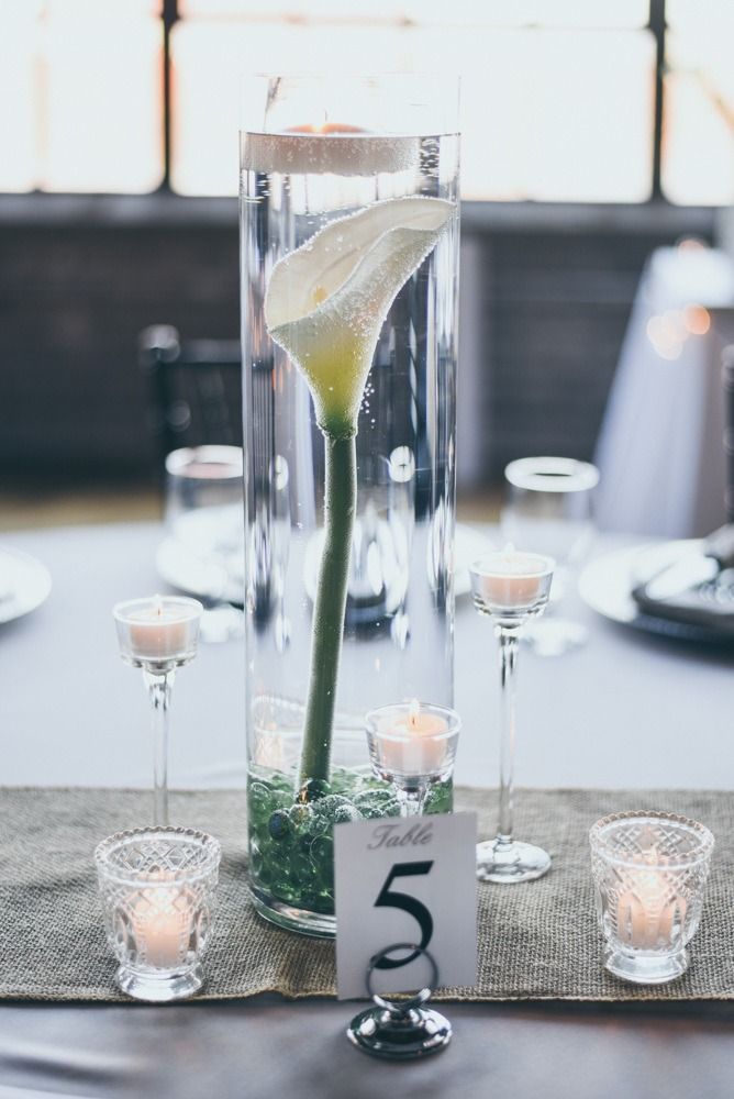Wedding table centerpiece with submerged calla lily in a tall vase, candles, and table number.