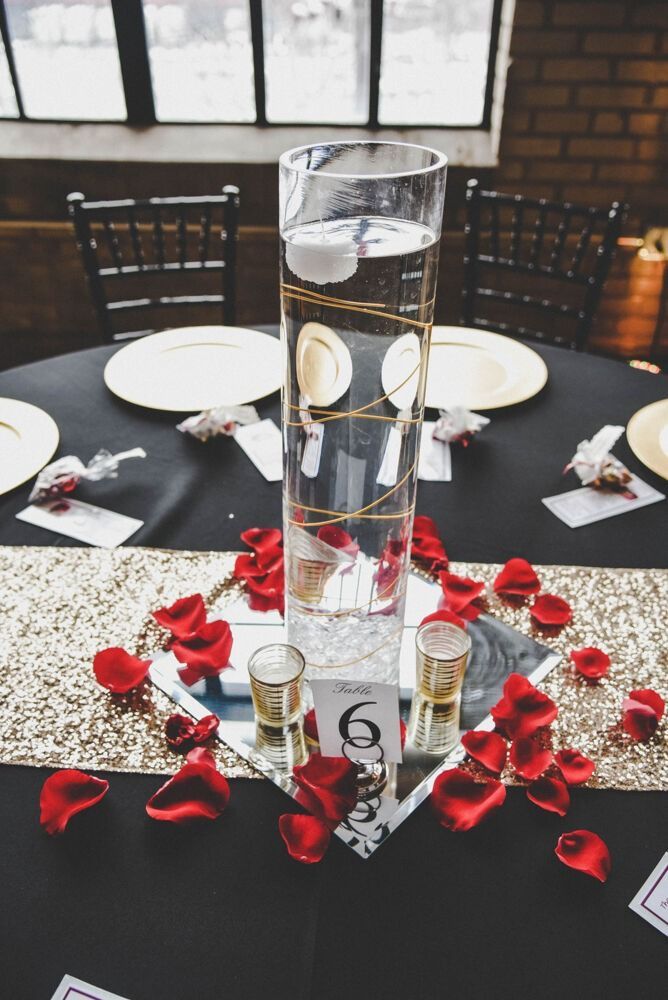 Wedding table centerpiece with tall vase, rose petals, gold accents, and a number 6.