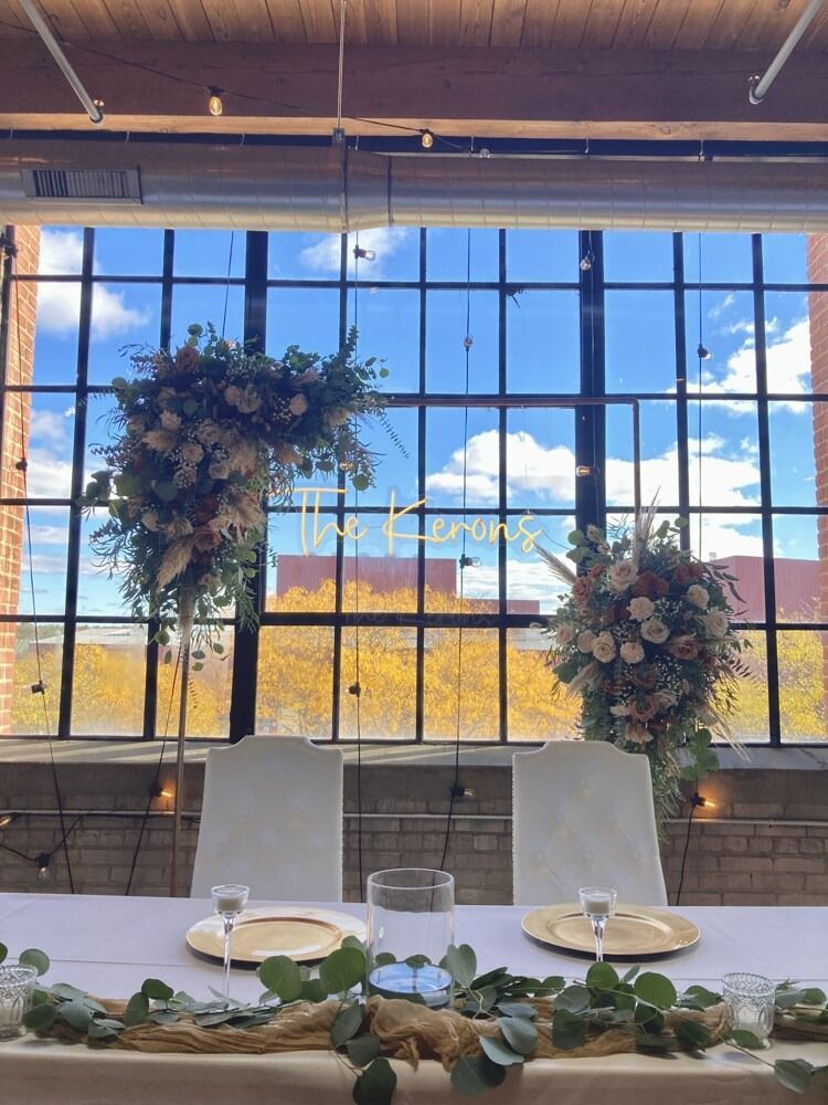 Wedding reception table with floral arrangements in front of large window, blue sky and yellow trees.