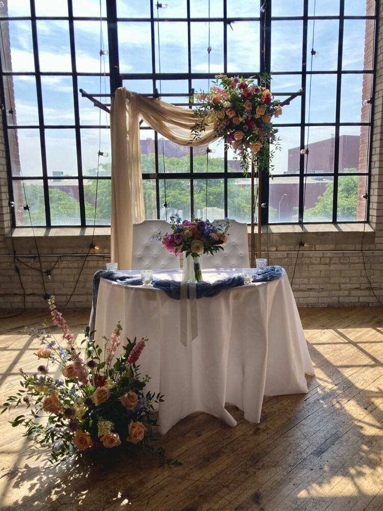 Wedding reception table with floral arrangements, white tablecloth, and window backdrop.