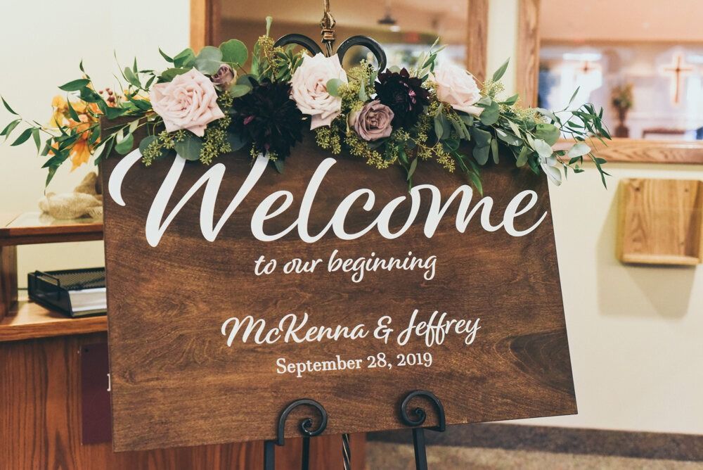 Welcome sign for a wedding. Wooden sign with floral arrangement. Says 