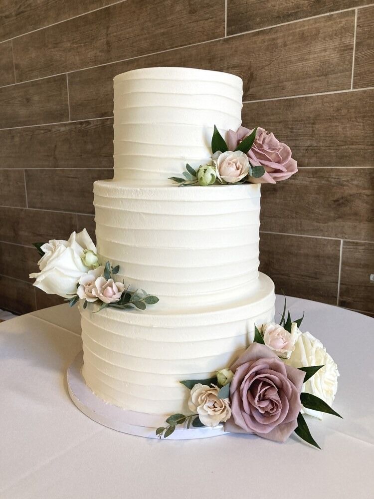 Three-tiered white cake with textured frosting and floral decorations on a white tablecloth.