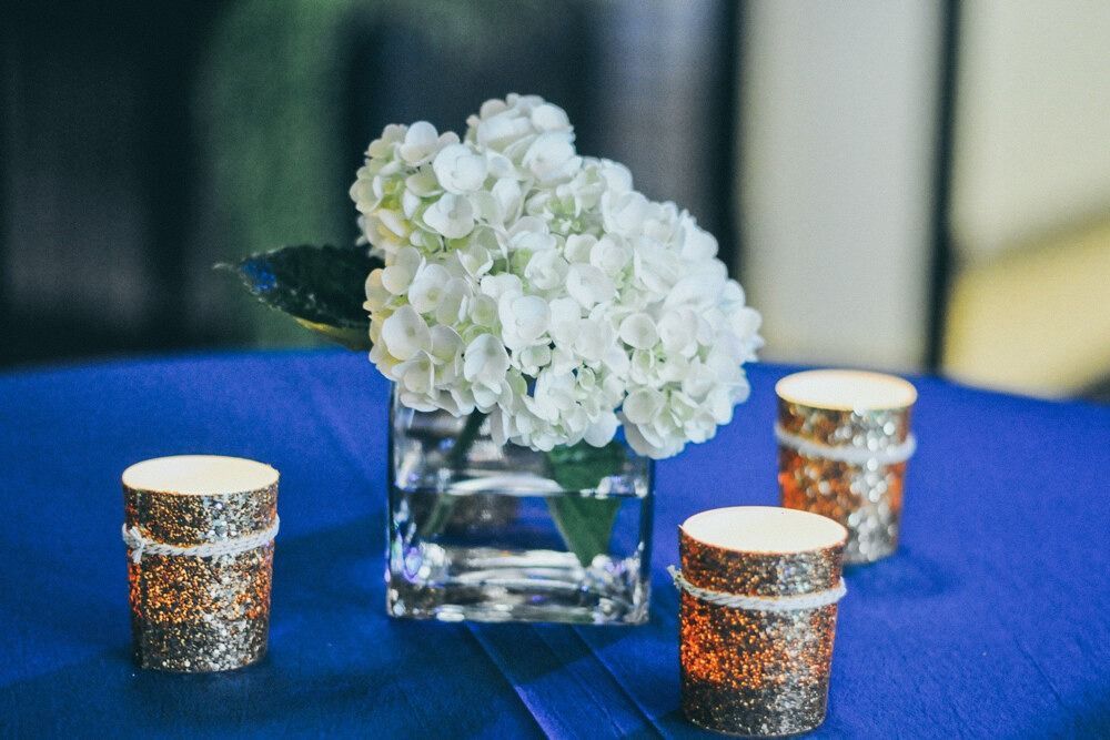 White hydrangea arrangement in glass vase with glitter candles on a blue tablecloth.