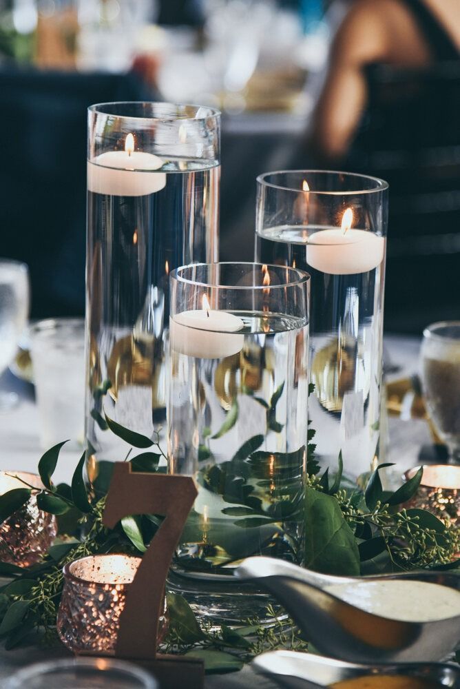 Centerpiece with floating candles in glass vases, greenery, and table number.