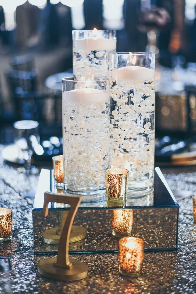 Gold and white wedding centerpiece with floating candles, votives, and table number on a mirrored base.