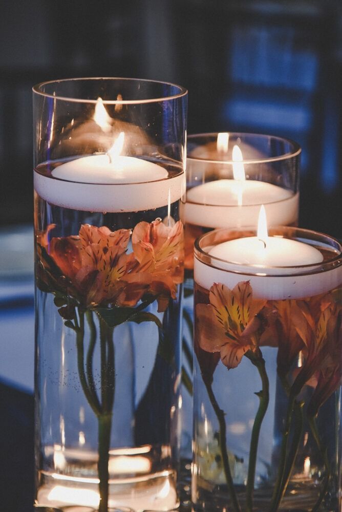 Three glass cylinders with floating candles, submerged flowers.