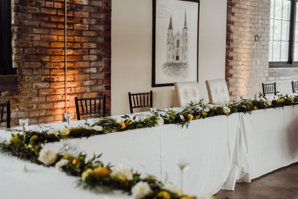 Long banquet table decorated with flowers in a room with exposed brick and an art print.