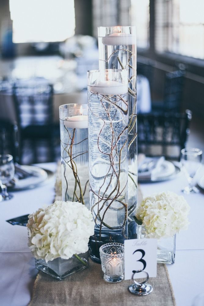Centerpiece: tall glass vases with floating candles, branches, and white flowers on a table.