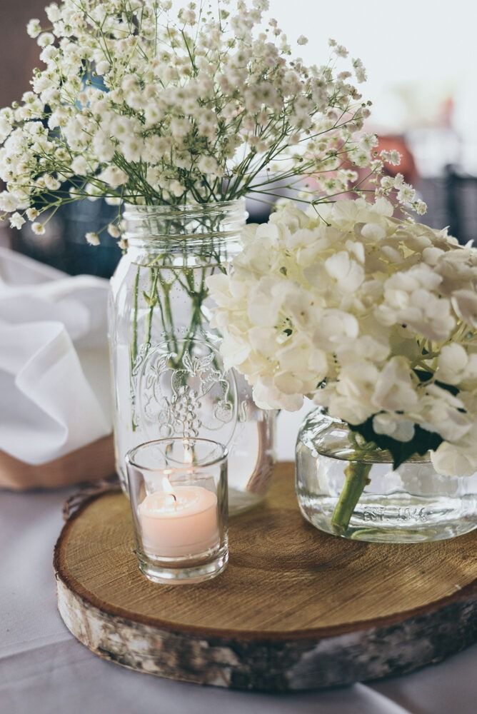 Centerpiece with white flowers in mason jars, votive candle, and wooden slice.