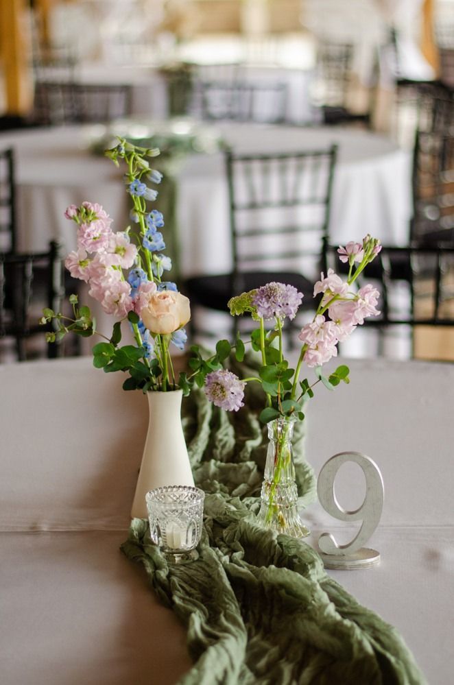 Floral centerpiece on a table, including pink and blue flowers, a candle, number 9, and green fabric.