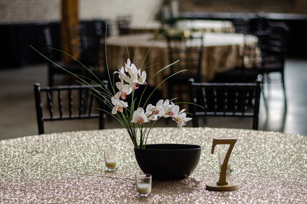 Table set for an event with gold sequin tablecloth, orchid centerpiece, and table number seven.