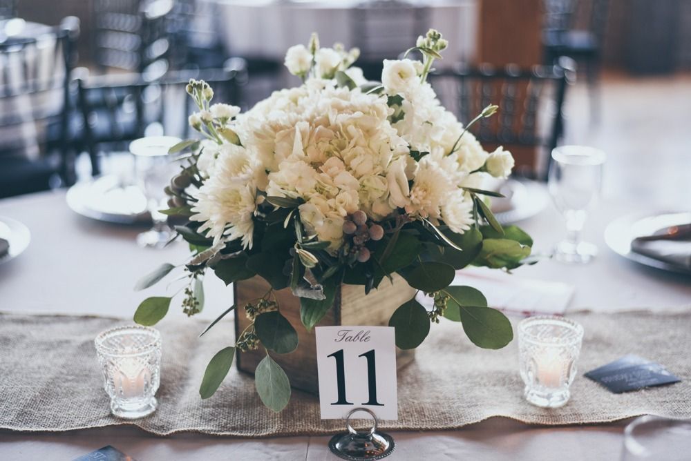 Table centerpiece with white flowers, table number 11, candles, and burlap runner.