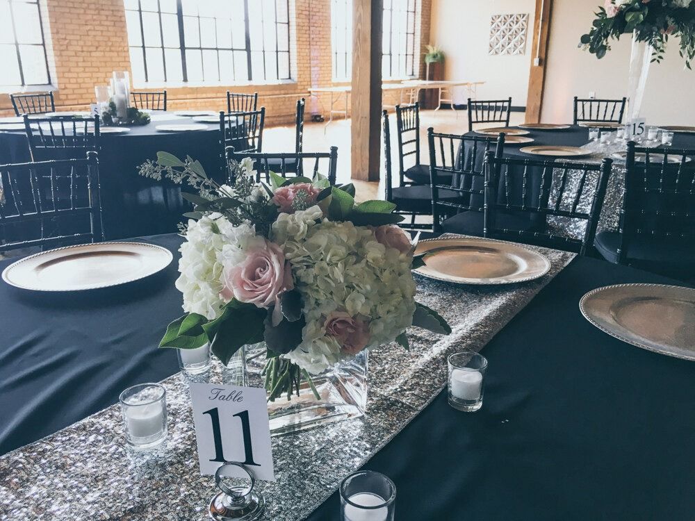 Formal dining table setting with floral centerpiece, navy tablecloth, silver charger plates, and table number 11.