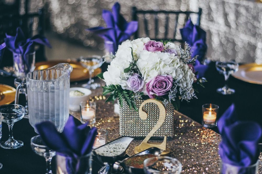 Formal table setting with floral centerpiece, purple napkins, and gold table number.