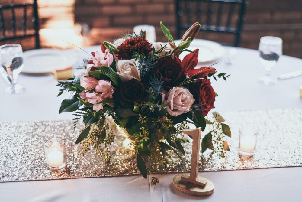 Centerpiece of flowers, roses, and greenery on a sequin table runner, at a reception with table number 1.