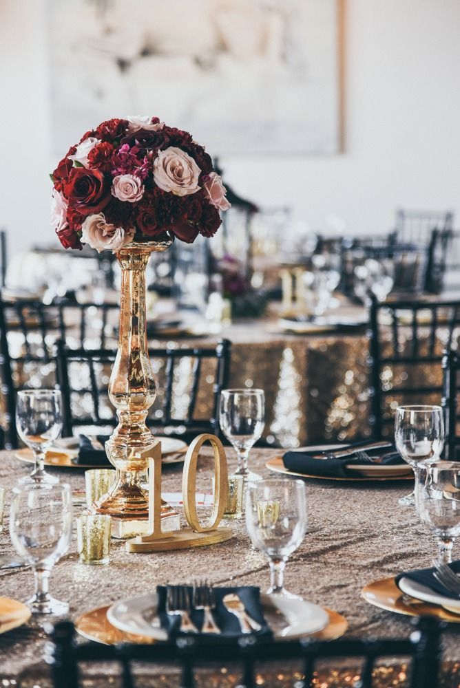 Gold-toned table setting with floral centerpiece, numbered table marker, and place settings.