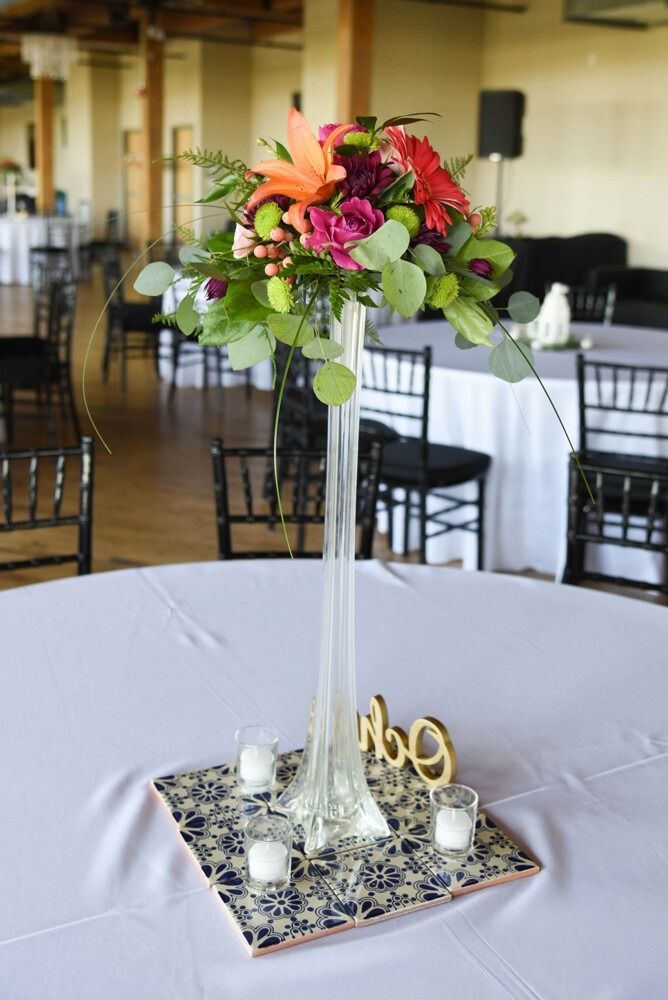 Tall floral centerpiece with vibrant flowers on a table, with candles and a table number.
