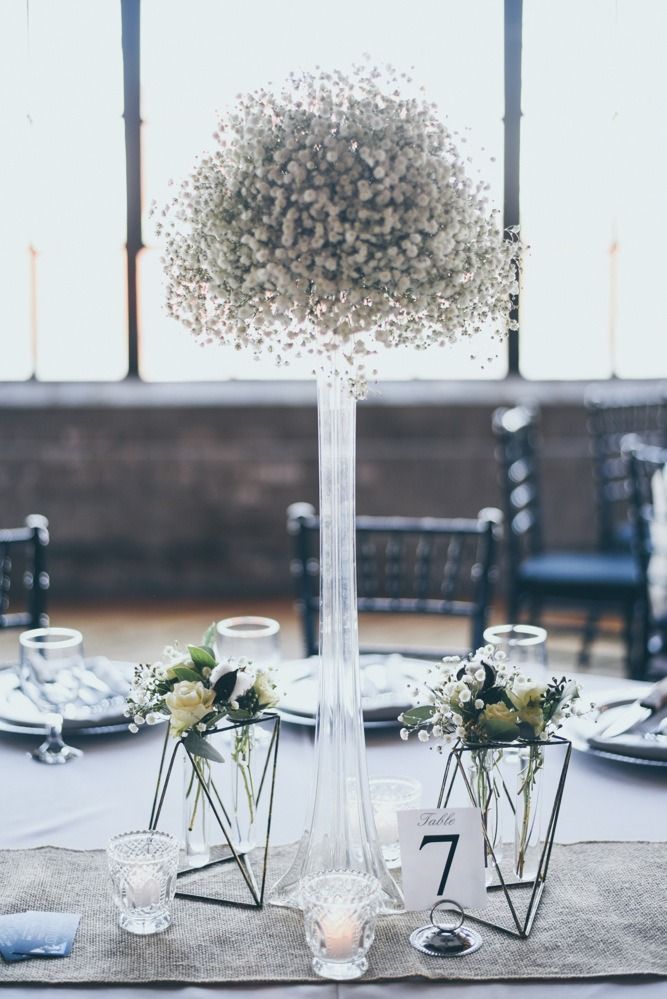 Wedding table setting with baby's breath floral arrangement. Tall vase centerpiece, geometric vases, and candles.