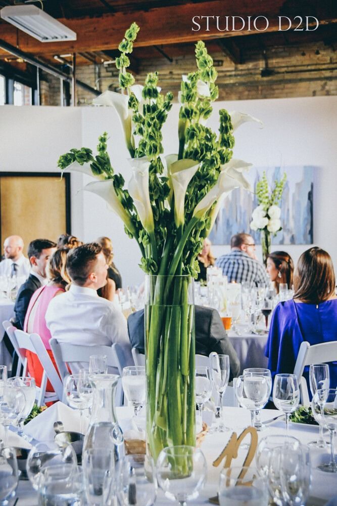 Tall floral centerpiece on table at a wedding reception; guests seated.