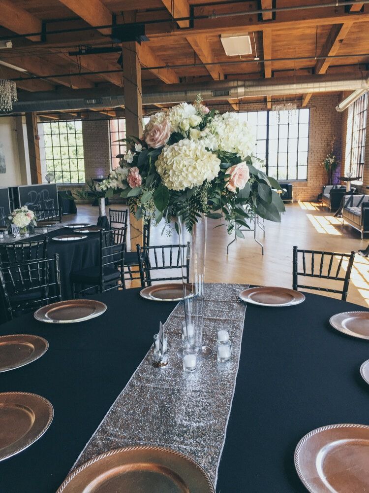 Wedding reception table with floral centerpiece, black tablecloth, gold charger plates, and silver runner.