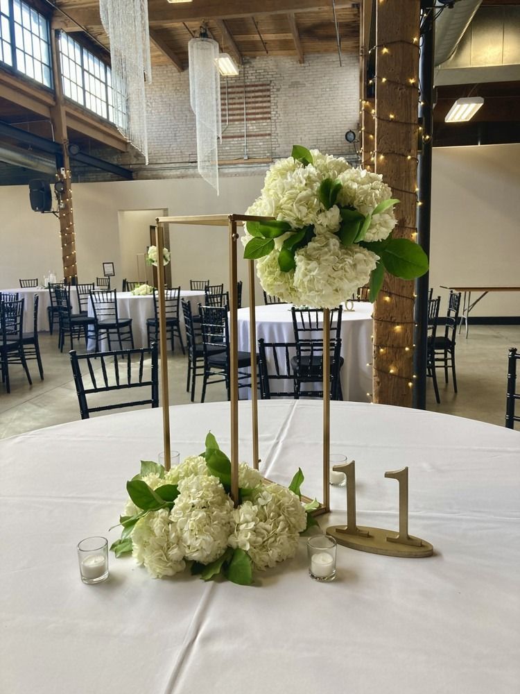 A wedding reception table with white hydrangea floral arrangement and gold geometric centerpieces.