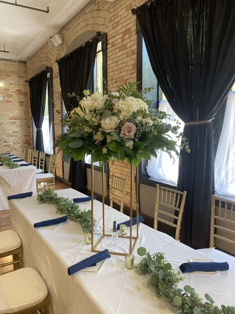 Long tables set for a wedding, with tall floral centerpiece and dark curtains.
