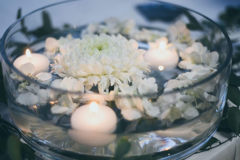 Glass bowl with water, white flowers, and floating candles.