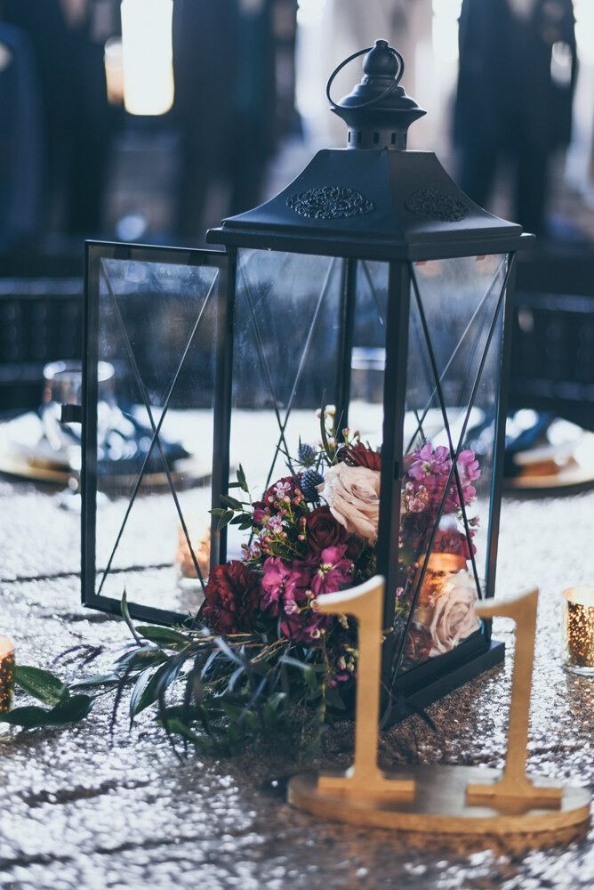 Black lantern centerpiece with flowers, gold table number eleven, on sequined tablecloth.